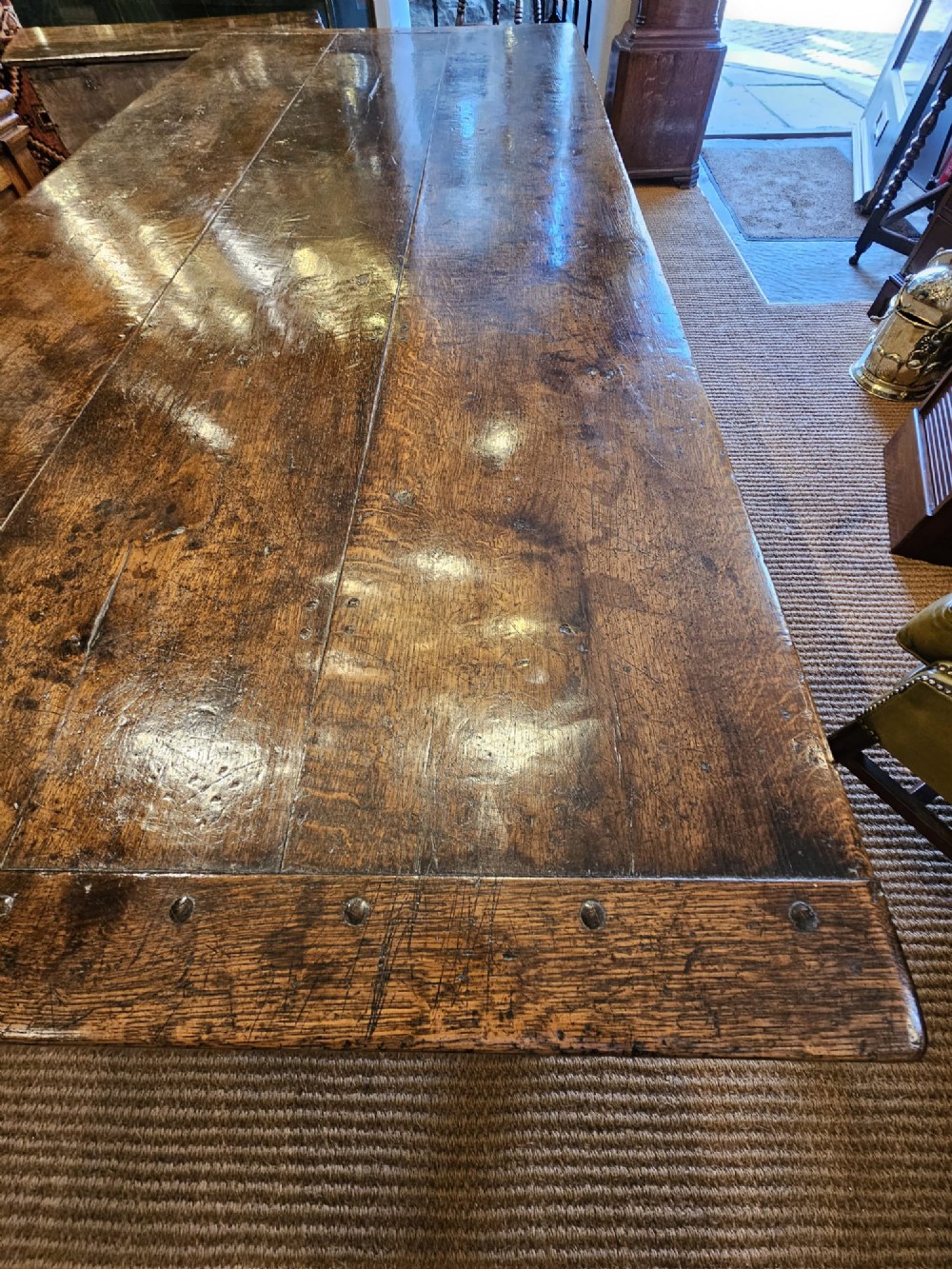 A large George III dark oak refectory dining table featuring a solid plank top, turned legs, and a low H-stretcher base. View XI