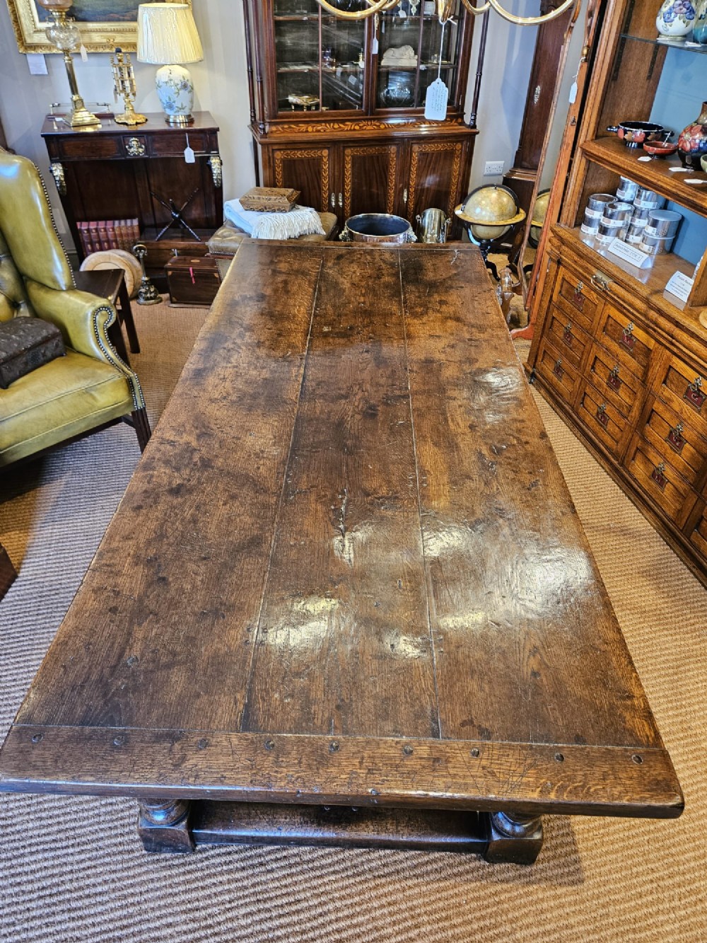 A large George III dark oak refectory dining table featuring a solid plank top, turned legs, and a low H-stretcher base. View XII