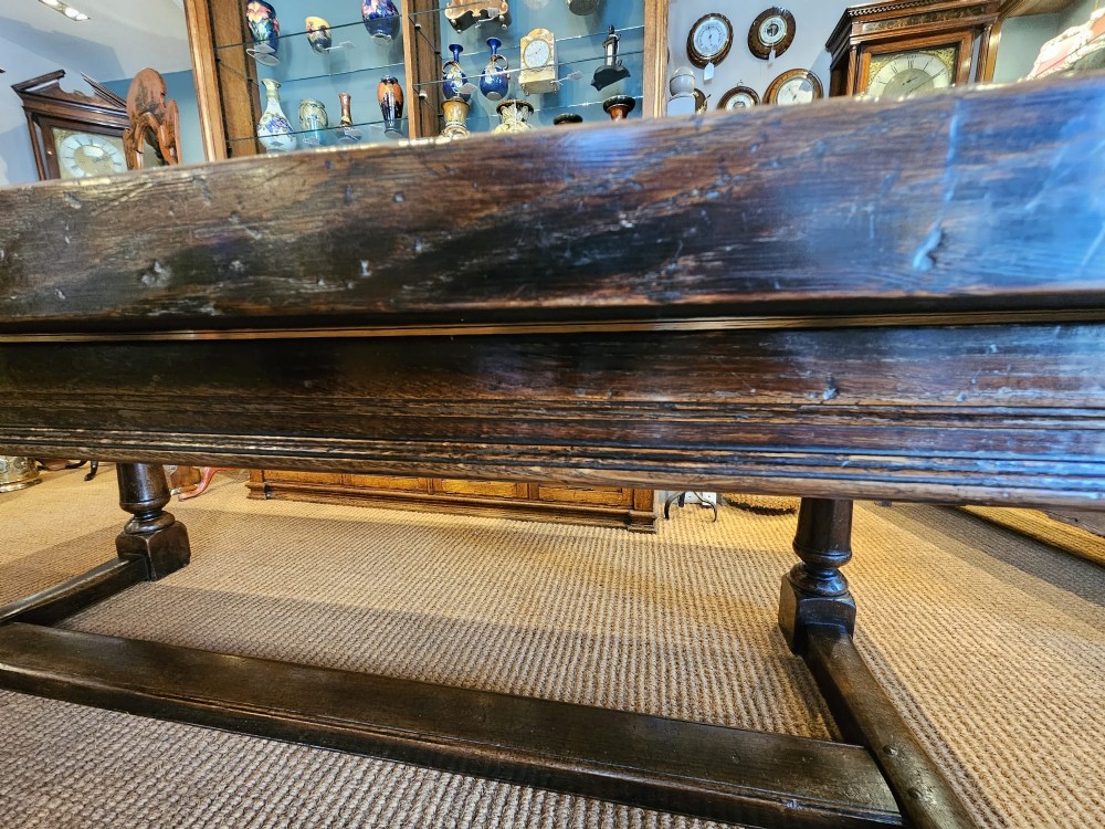 A large George III dark oak refectory dining table featuring a solid plank top, turned legs, and a low H-stretcher base. View XIII