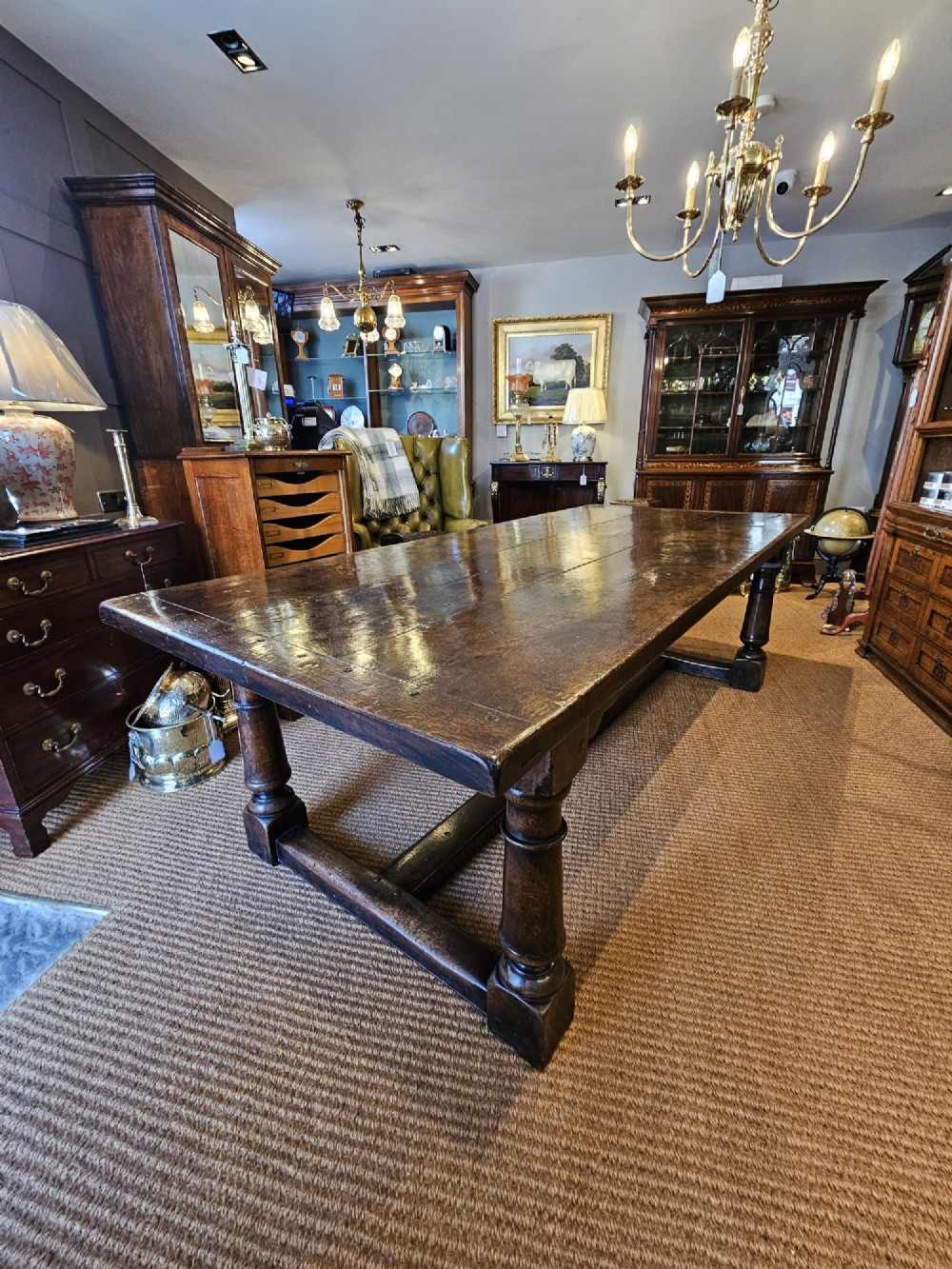 A large George III dark oak refectory dining table featuring a solid plank top, turned legs, and a low H-stretcher base. View XIV