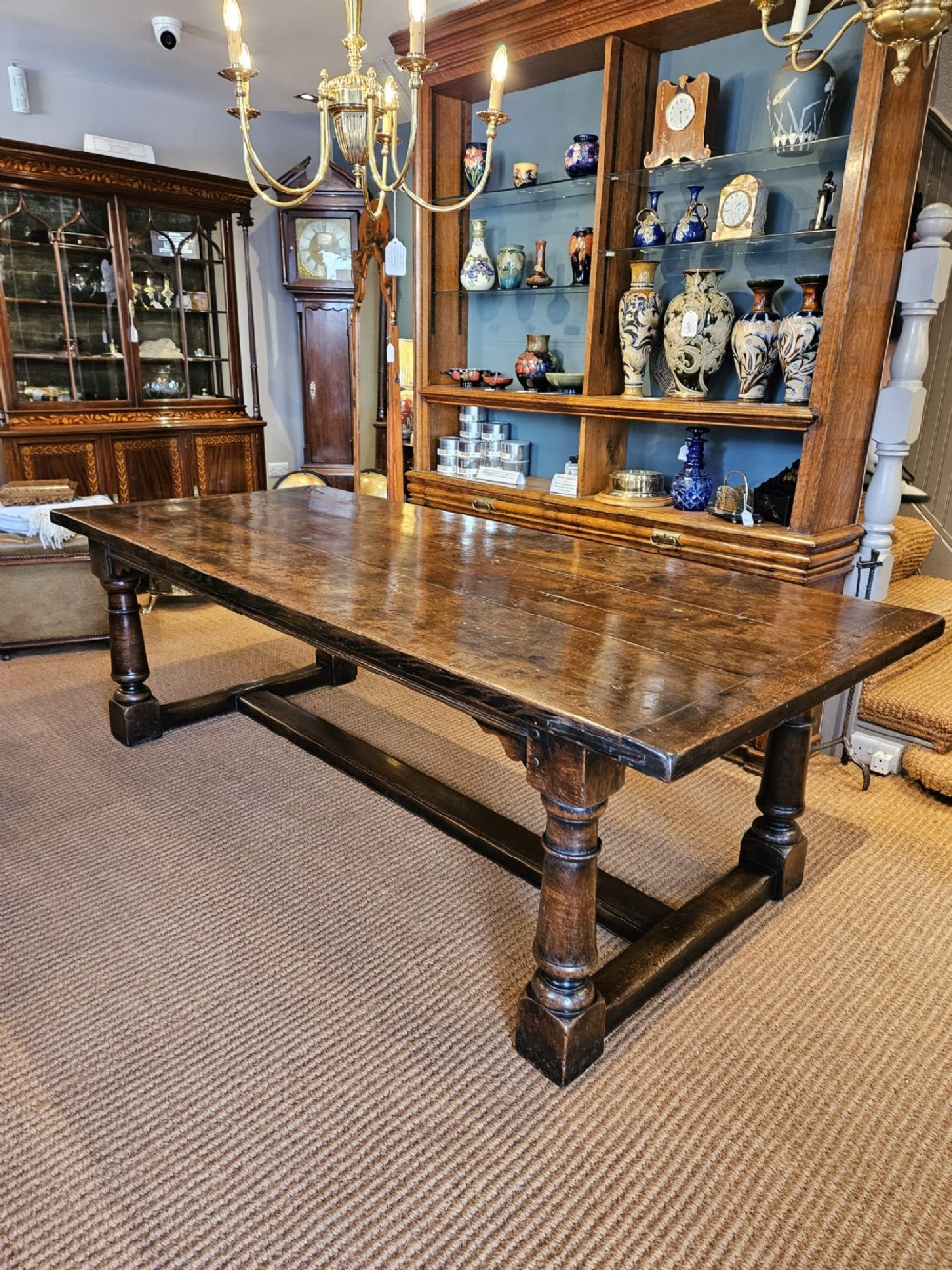 A large George III dark oak refectory dining table featuring a solid plank top, turned legs, and a low H-stretcher base. View XV