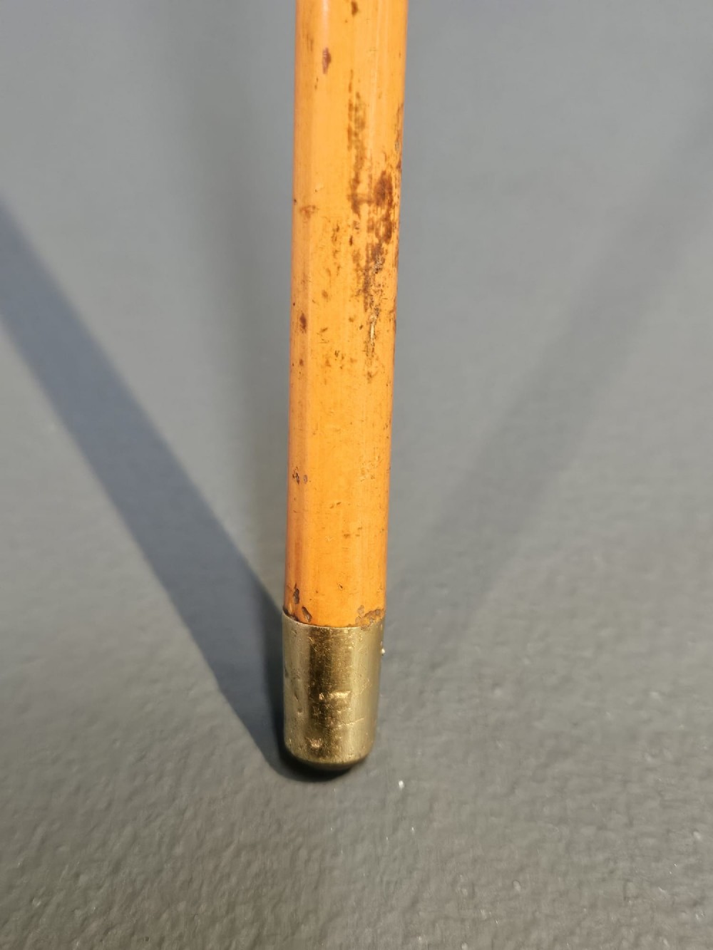 A slender light brown wooden swagger stick featuring a polished gold top inset with a small red ruby. View II