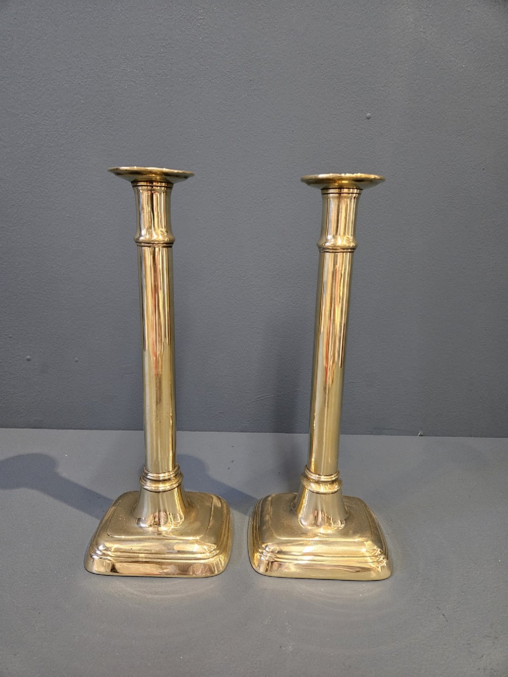 A pair of tall George III brass candlesticks with stepped square bases and slender cylindrical columns featuring raised band details.