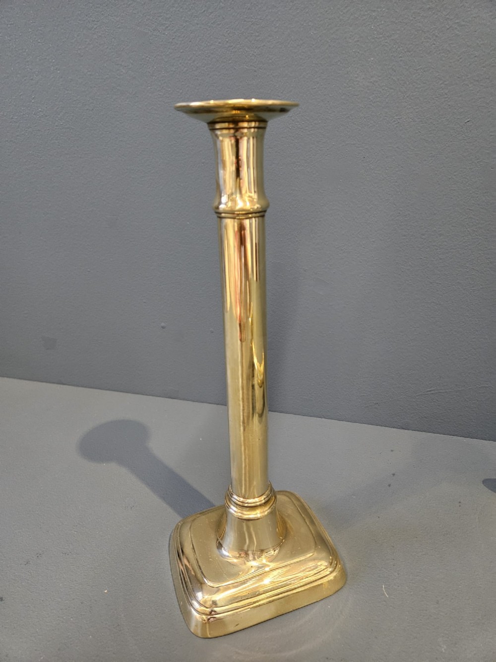 A pair of tall George III brass candlesticks with stepped square bases and slender cylindrical columns featuring raised band details. View IV