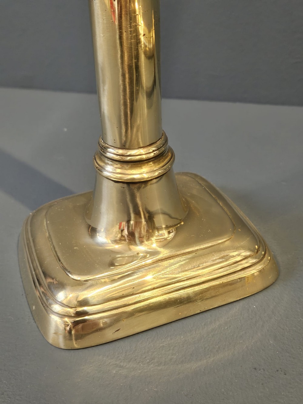 A pair of tall George III brass candlesticks with stepped square bases and slender cylindrical columns featuring raised band details. View V