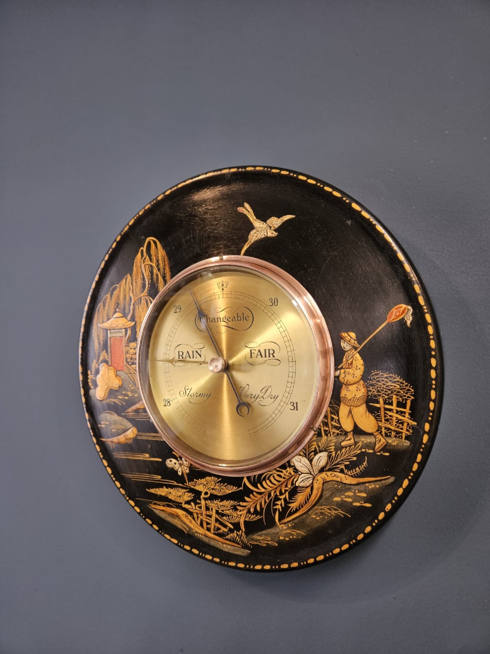 A circular Edwardian aneroid barometer set in a black lacquered frame with gilded hand-painted Chinoiserie figures and landscape motifs. View II