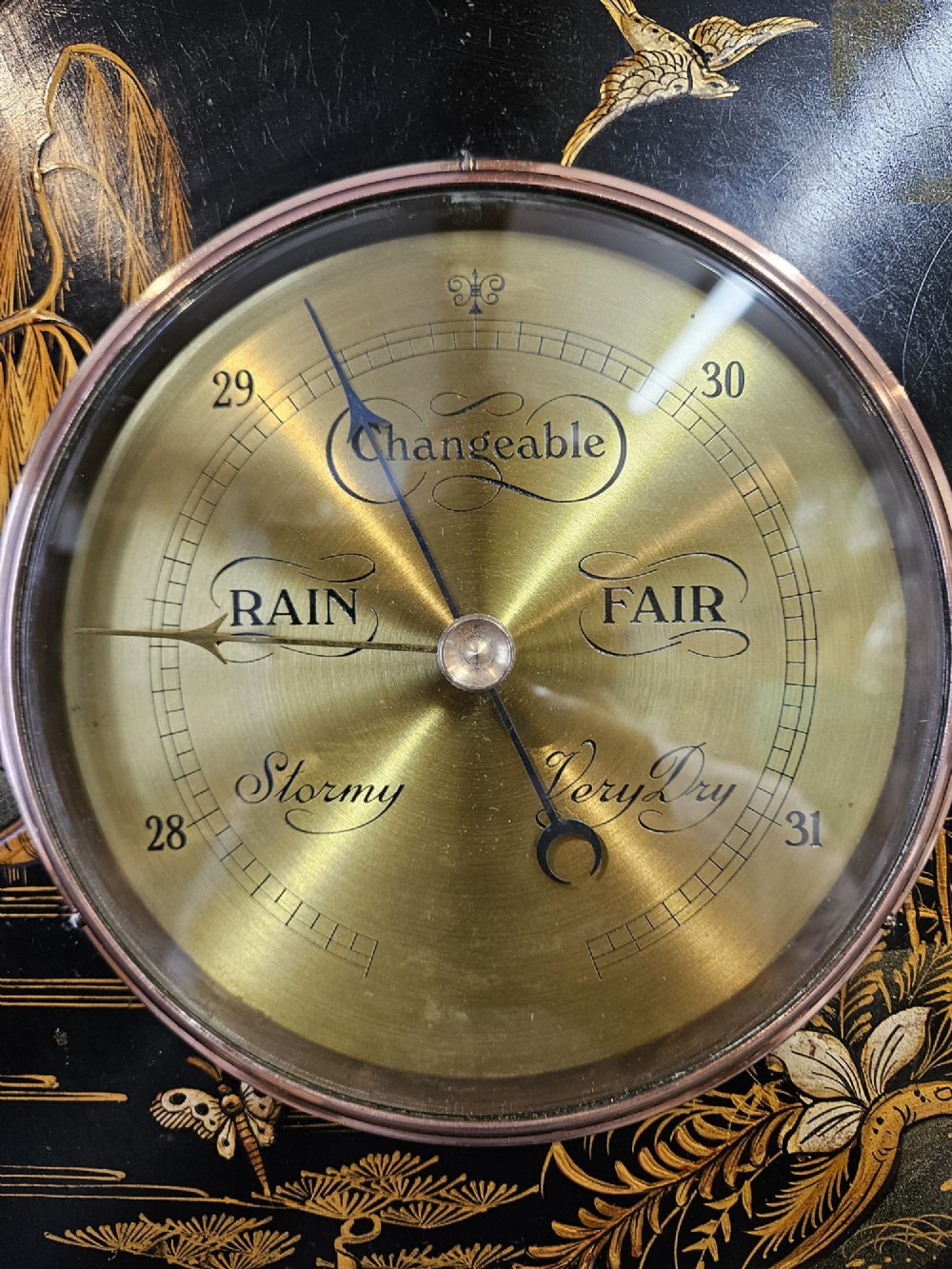 A circular Edwardian aneroid barometer set in a black lacquered frame with gilded hand-painted Chinoiserie figures and landscape motifs. View III