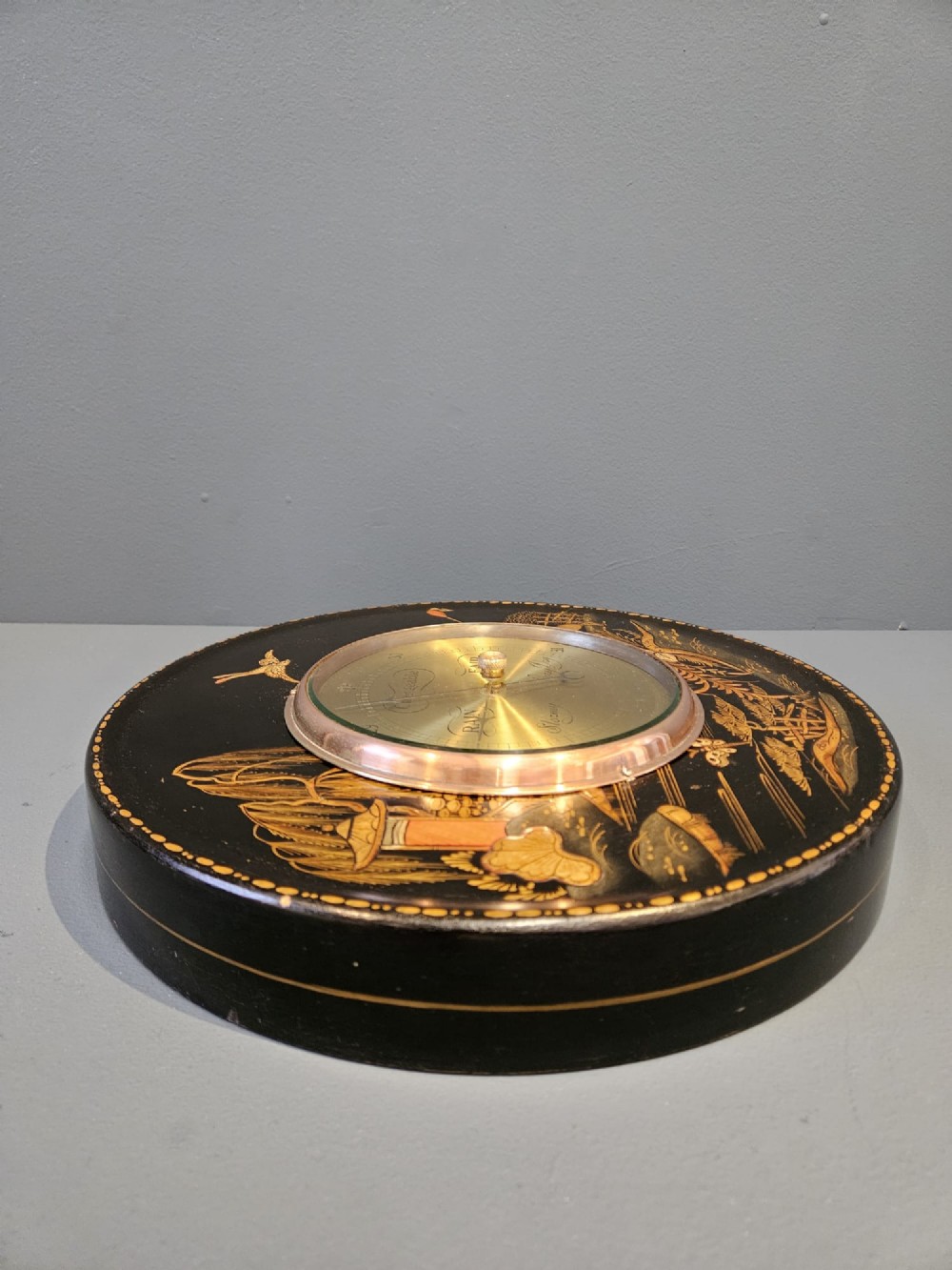 A circular Edwardian aneroid barometer set in a black lacquered frame with gilded hand-painted Chinoiserie figures and landscape motifs. View IV