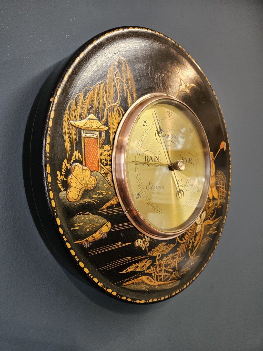 A circular Edwardian aneroid barometer set in a black lacquered frame with gilded hand-painted Chinoiserie figures and landscape motifs. View V
