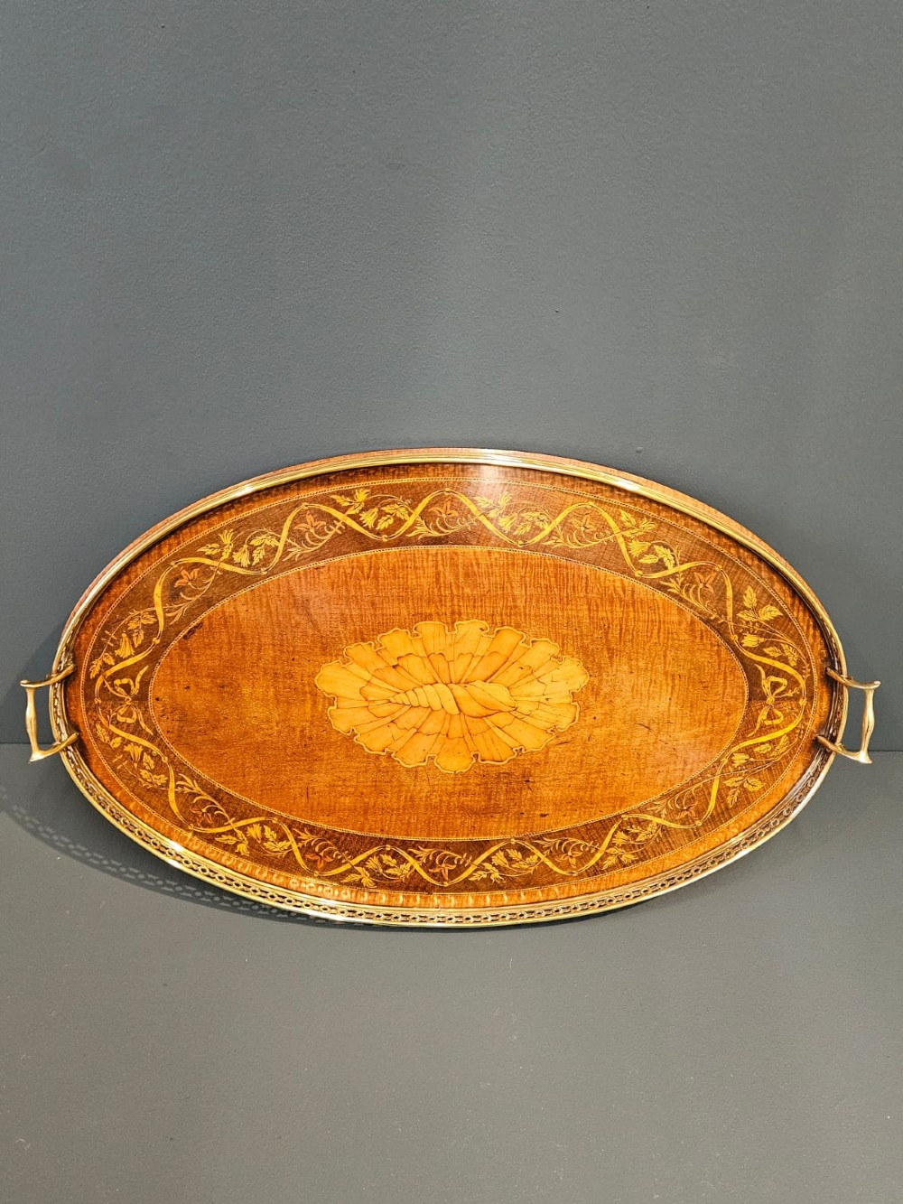 An oval Victorian mahogany serving tray featuring detailed floral marquetry inlay, a central shell motif, and a pierced brass gallery rim with two handles. View II