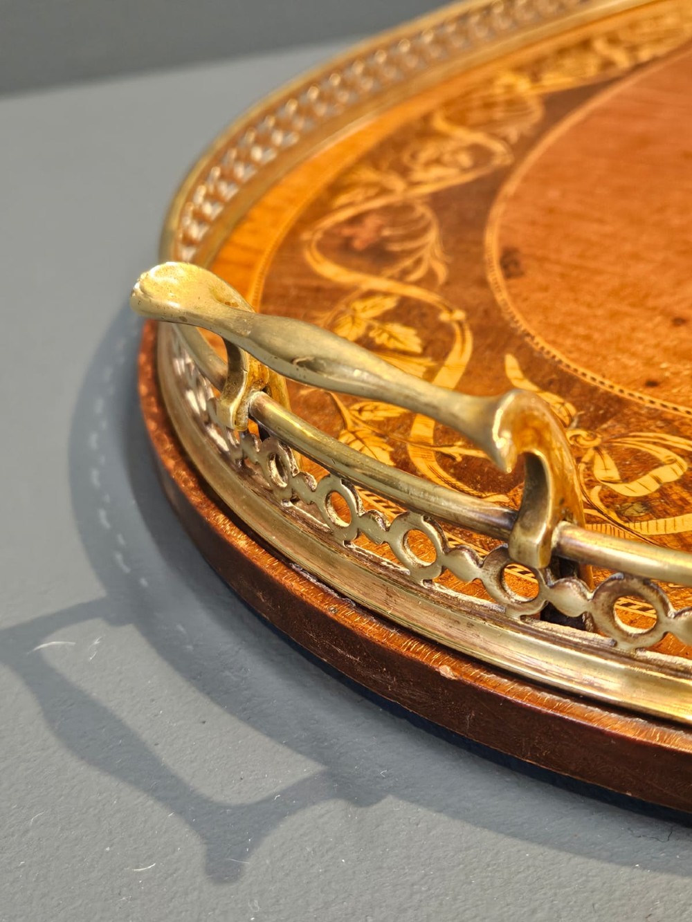 An oval Victorian mahogany serving tray featuring detailed floral marquetry inlay, a central shell motif, and a pierced brass gallery rim with two handles. View VI