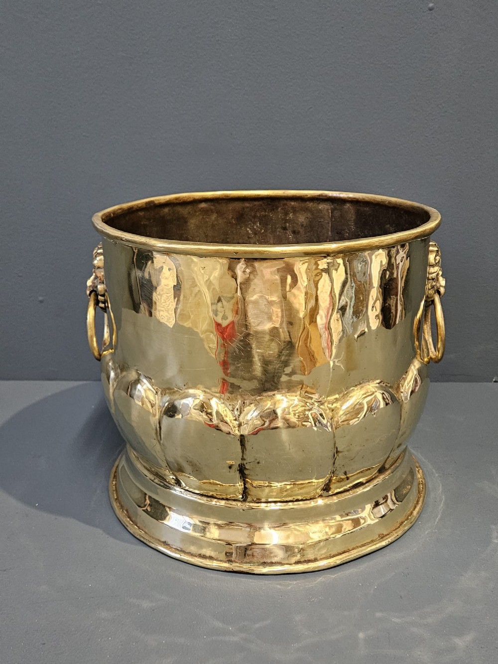 A Victorian brass planter featuring a polished finish, lobed lower body, and cast lion mask ring handles. View II