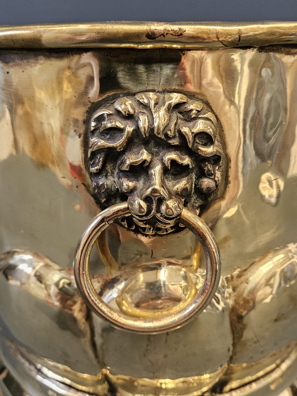 A Victorian brass planter featuring a polished finish, lobed lower body, and cast lion mask ring handles. View VI