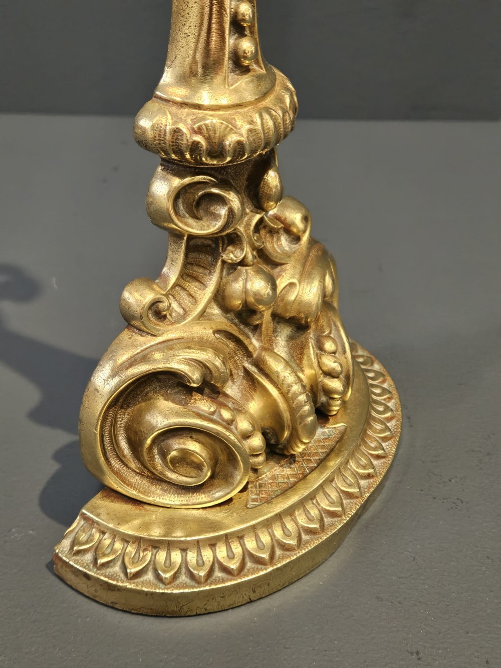An ornate Victorian cast brass door stop featuring a top ring handle, a tapered column with scrollwork, and a weighted semi-circular base. View II