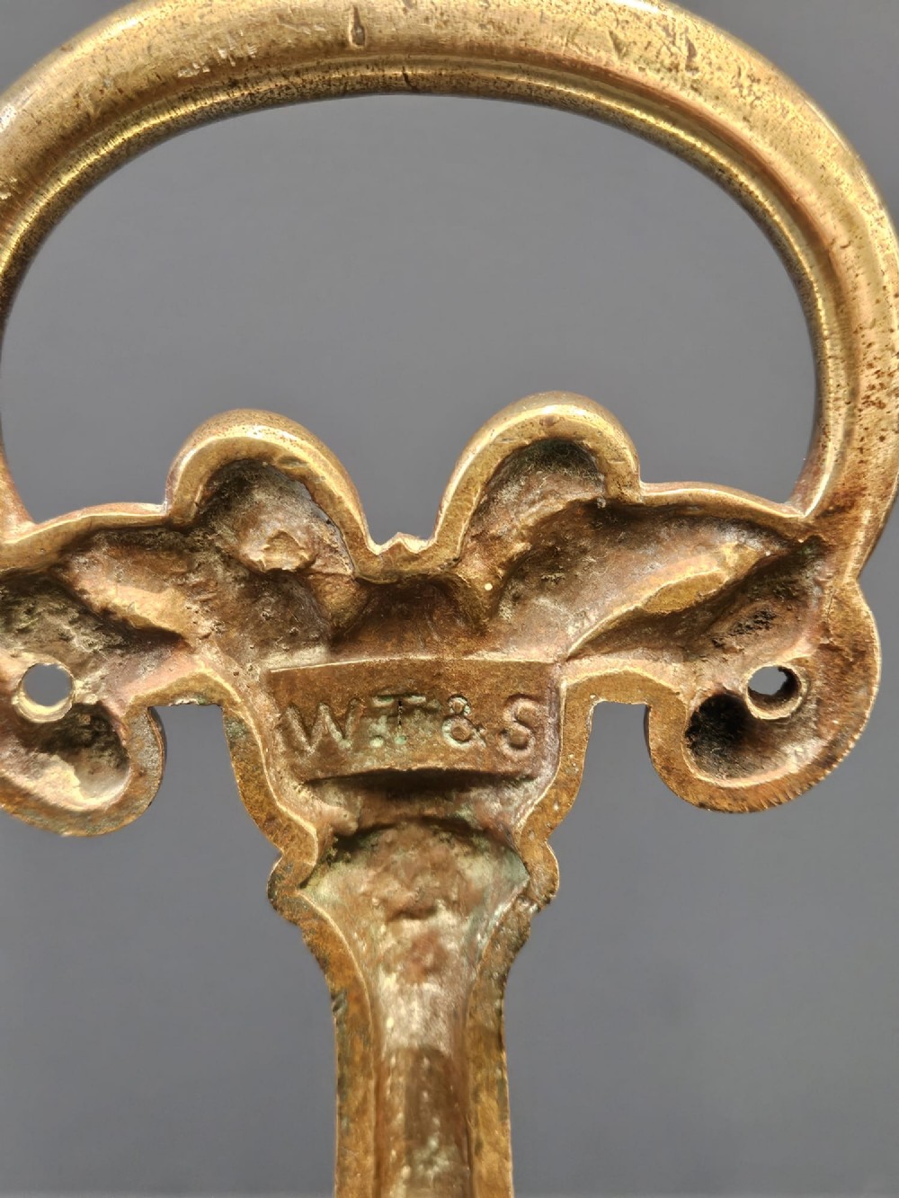 An ornate Victorian cast brass door stop featuring a top ring handle, a tapered column with scrollwork, and a weighted semi-circular base. View VI