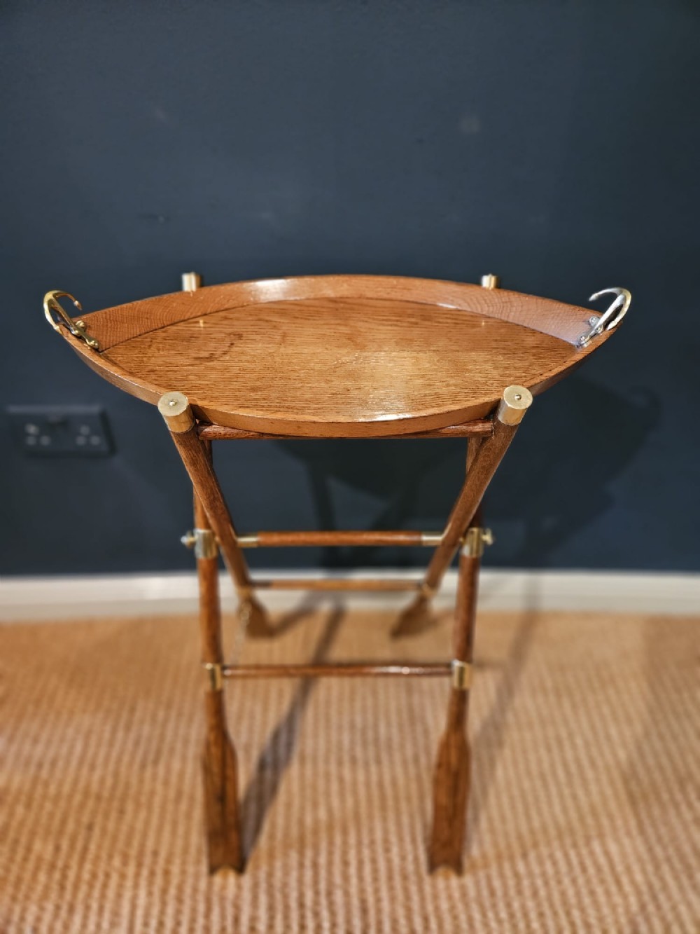 A boat-shaped oak tray with brass handles resting on a folding wooden stand constructed from crossed oars.
