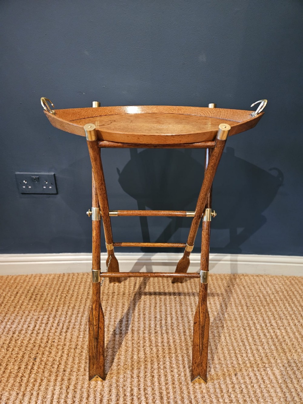 A boat-shaped oak tray with brass handles resting on a folding wooden stand constructed from crossed oars. View II