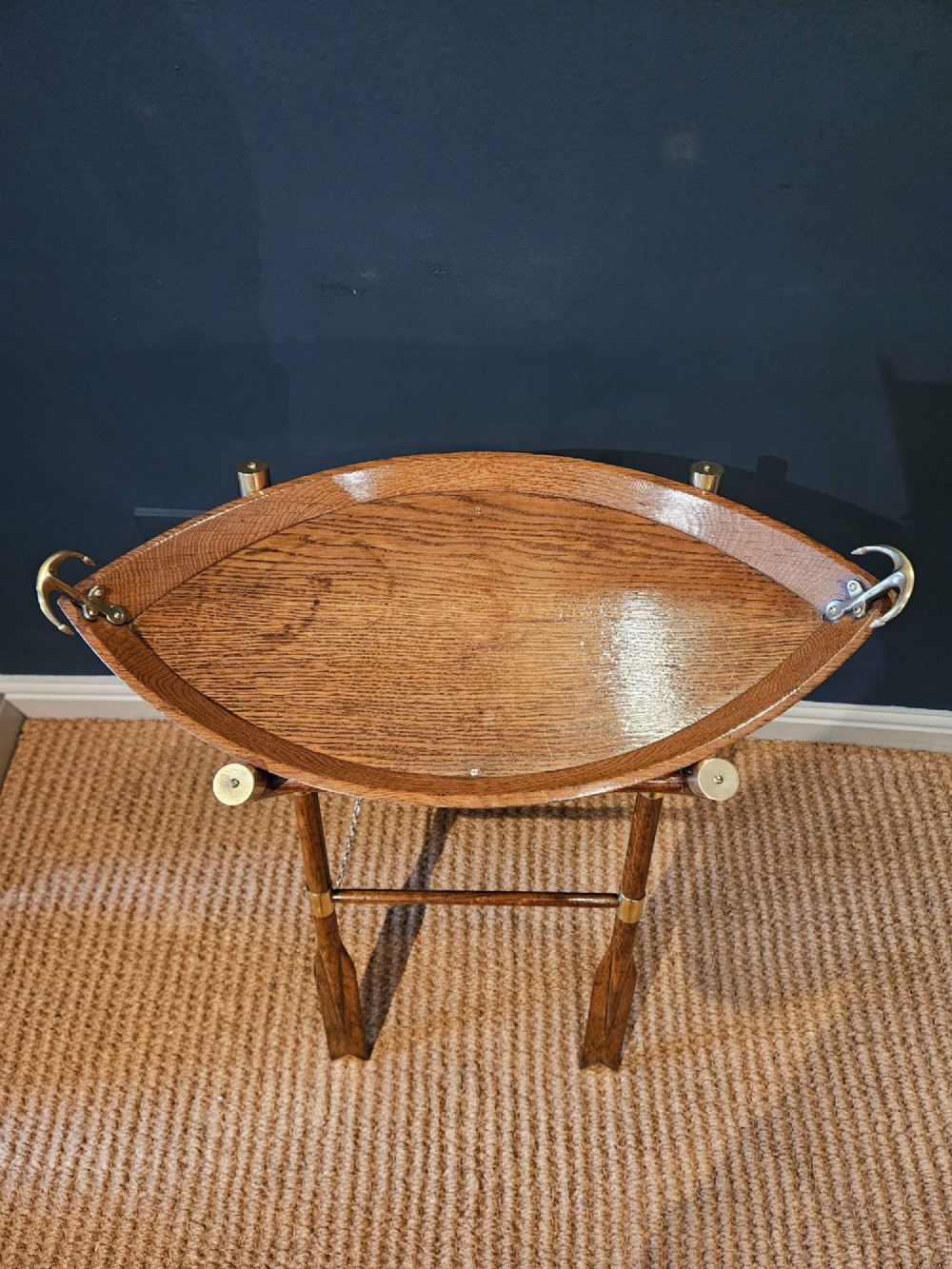 A boat-shaped oak tray with brass handles resting on a folding wooden stand constructed from crossed oars. View IV