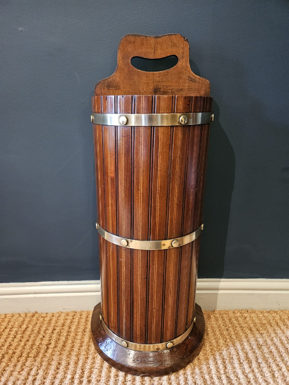 A cylindrical reeded mahogany stick stand featuring brass binding bands and a carved cut-out carrying handle. View II