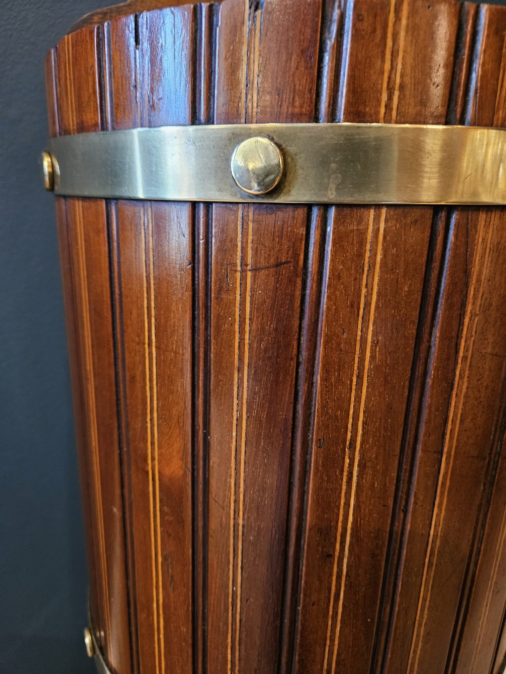 A cylindrical reeded mahogany stick stand featuring brass binding bands and a carved cut-out carrying handle. View III