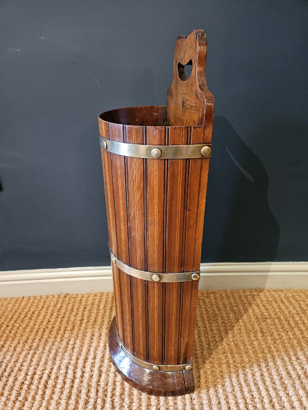A cylindrical reeded mahogany stick stand featuring brass binding bands and a carved cut-out carrying handle. View VIII