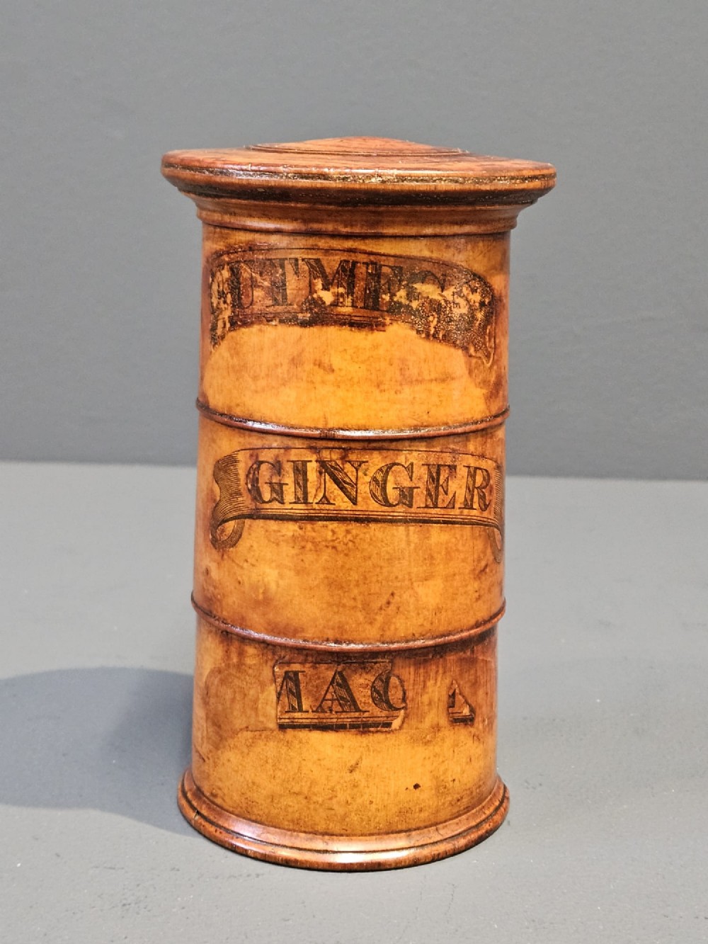 A cylindrical turned fruitwood spice tower featuring stacked compartments labelled Nutmeg, Ginger, and Mace.