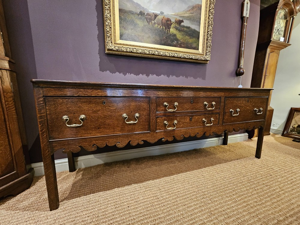 An eighteenth-century George III oak low dresser base featuring four drawers with brass swan-neck handles and a scalloped lower frieze.