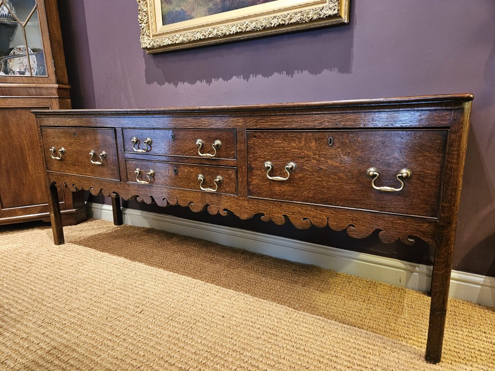 An eighteenth-century George III oak low dresser base featuring four drawers with brass swan-neck handles and a scalloped lower frieze. View II