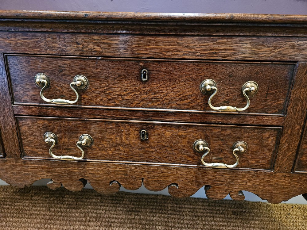 An eighteenth-century George III oak low dresser base featuring four drawers with brass swan-neck handles and a scalloped lower frieze. View III