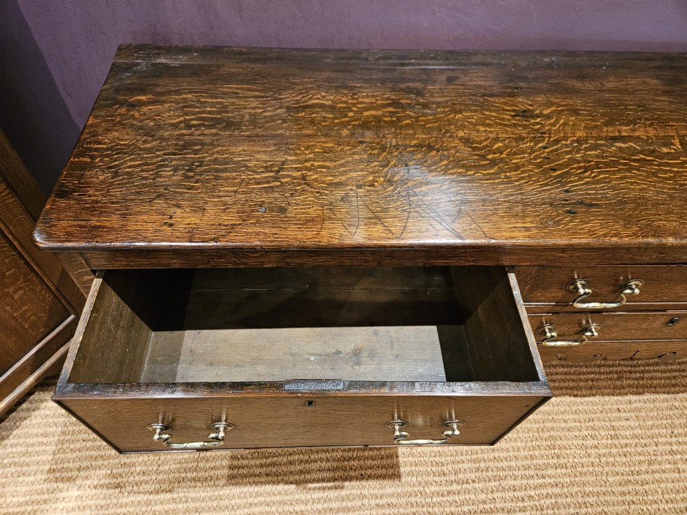 An eighteenth-century George III oak low dresser base featuring four drawers with brass swan-neck handles and a scalloped lower frieze. View IV
