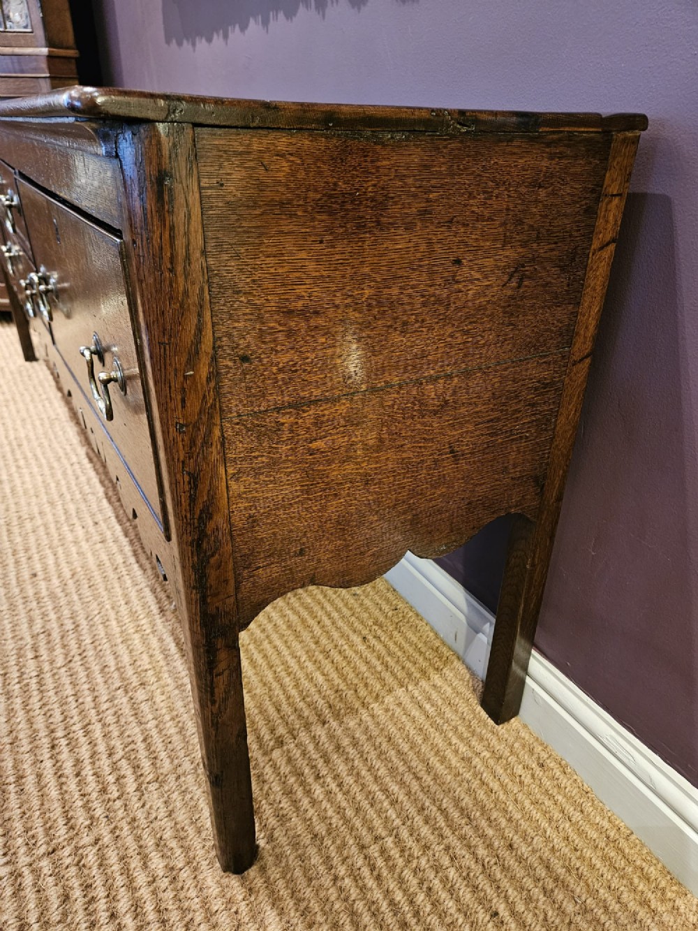 An eighteenth-century George III oak low dresser base featuring four drawers with brass swan-neck handles and a scalloped lower frieze. View V