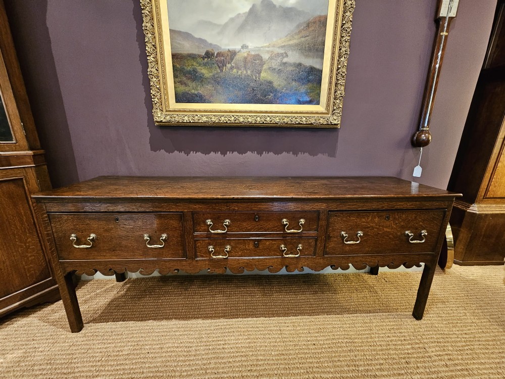 An eighteenth-century George III oak low dresser base featuring four drawers with brass swan-neck handles and a scalloped lower frieze. View VI