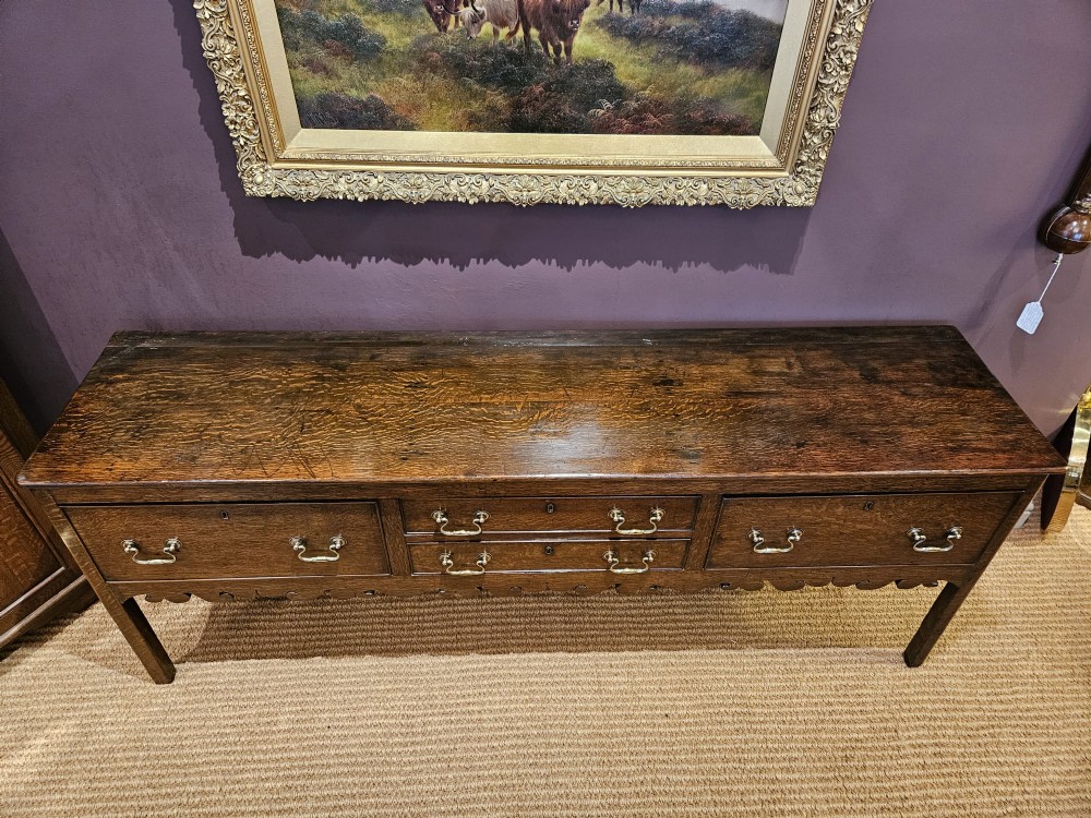 An eighteenth-century George III oak low dresser base featuring four drawers with brass swan-neck handles and a scalloped lower frieze. View VII
