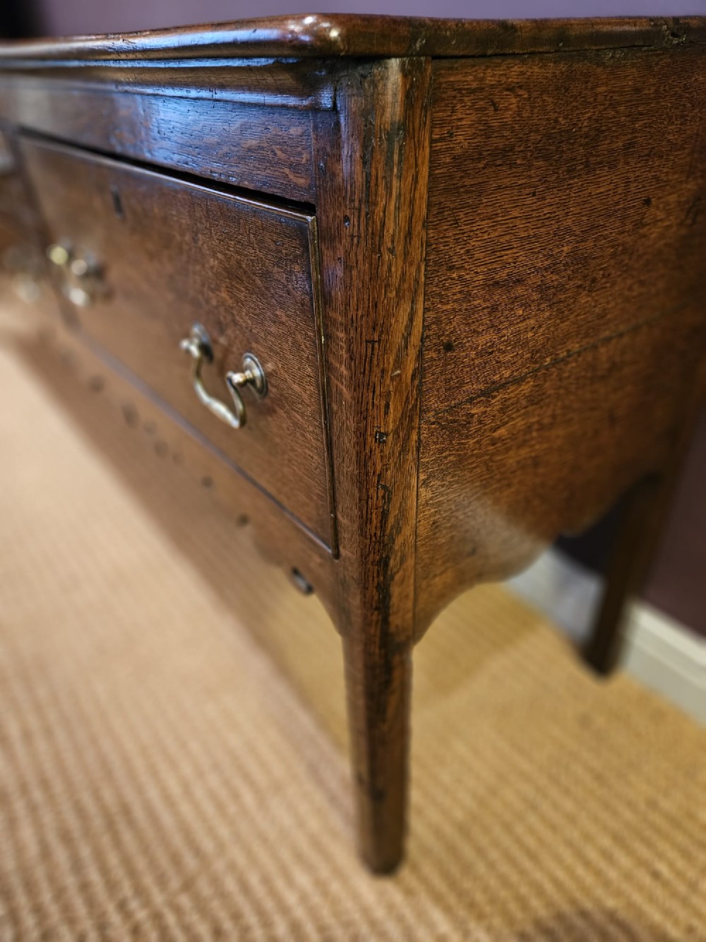 An eighteenth-century George III oak low dresser base featuring four drawers with brass swan-neck handles and a scalloped lower frieze. View X