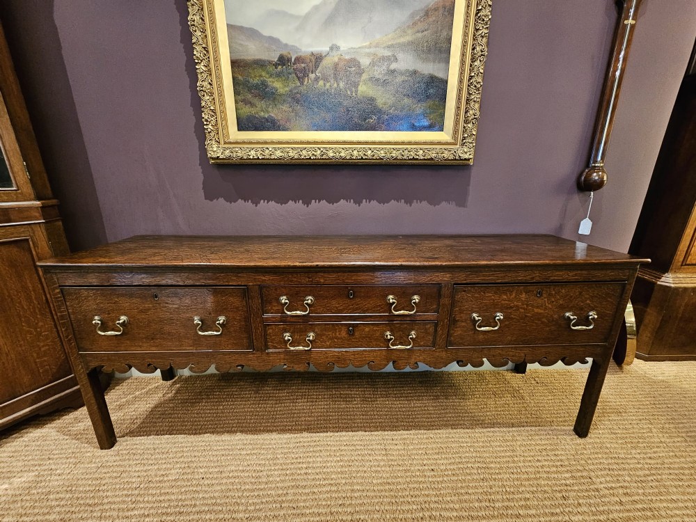 An eighteenth-century George III oak low dresser base featuring four drawers with brass swan-neck handles and a scalloped lower frieze. View XI