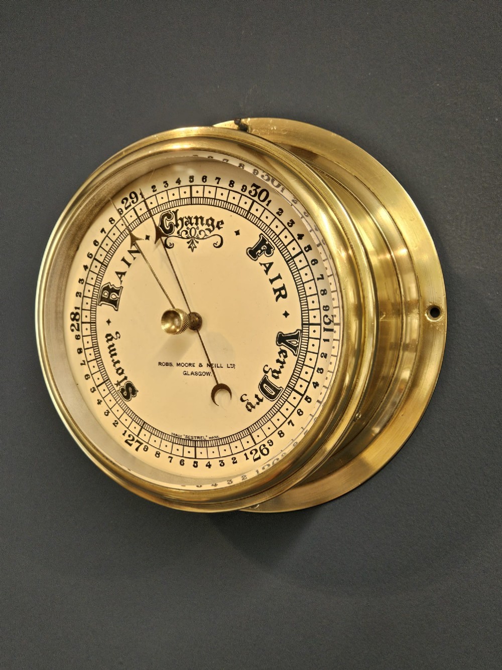 An Edwardian circular brass bulkhead barometer featuring a cream dial with black scale markings, typography, and two pointer hands under a clear glass cover. View II