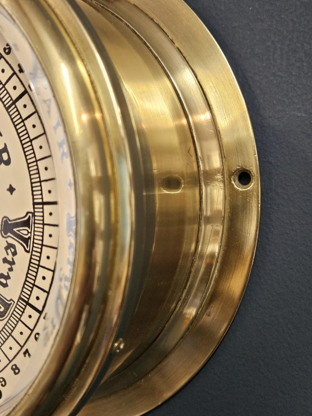 An Edwardian circular brass bulkhead barometer featuring a cream dial with black scale markings, typography, and two pointer hands under a clear glass cover. View III