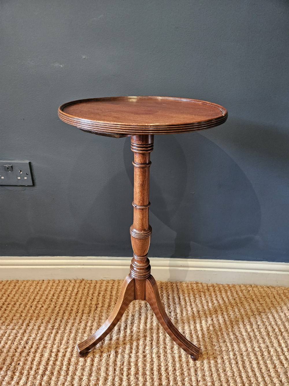 A George III mahogany wine table featuring a dished circular top, a turned central column, and a tripod base with three splayed legs.