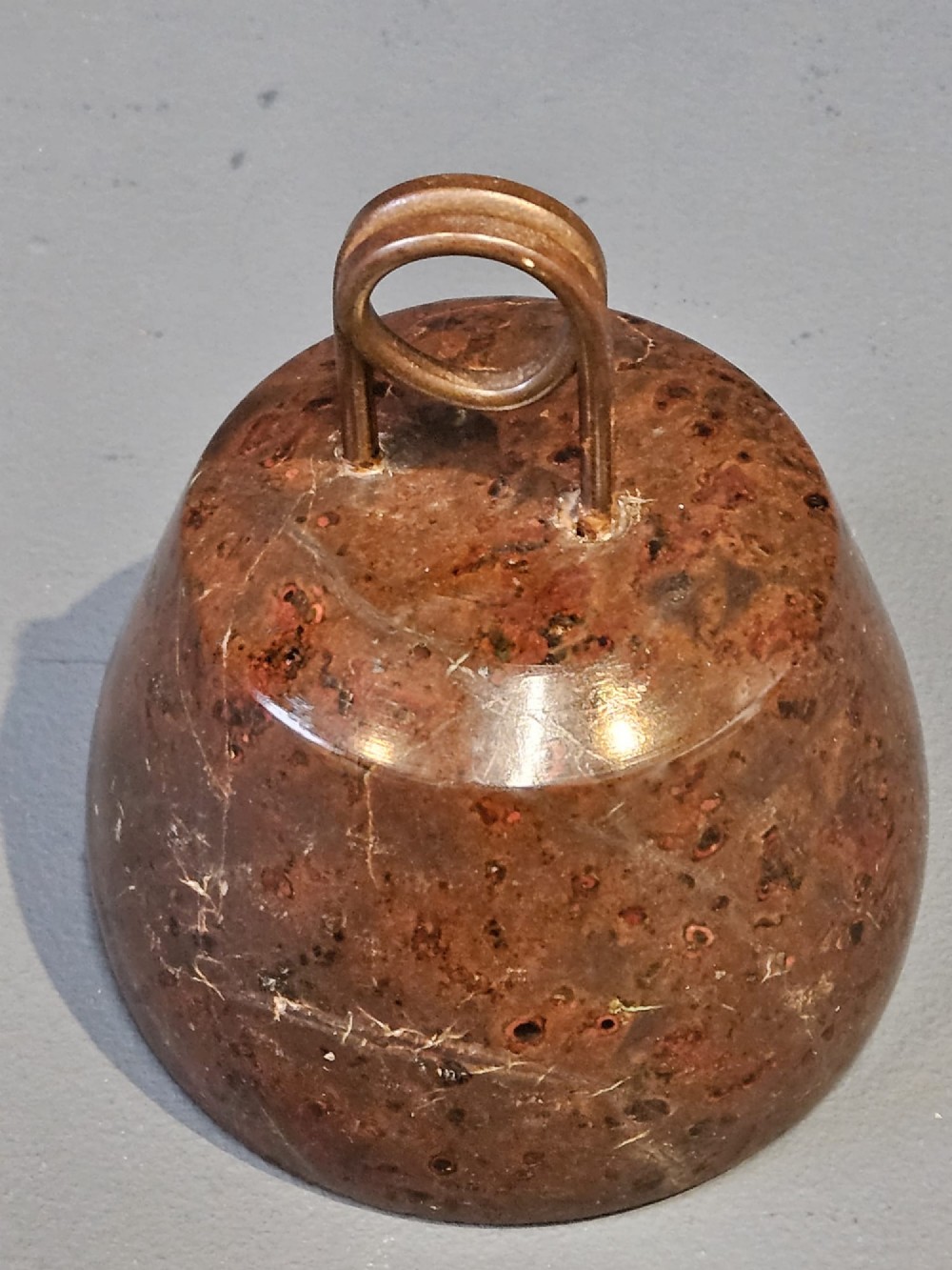 A turned bell-shaped red brown mottled serpentine stone door stop featuring a metal looped wire handle at the top. View III