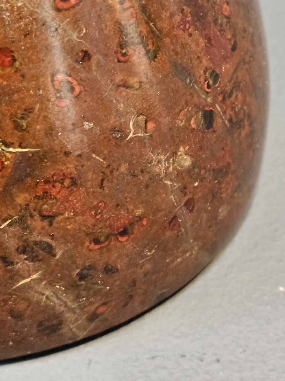 A turned bell-shaped red brown mottled serpentine stone door stop featuring a metal looped wire handle at the top. View IV