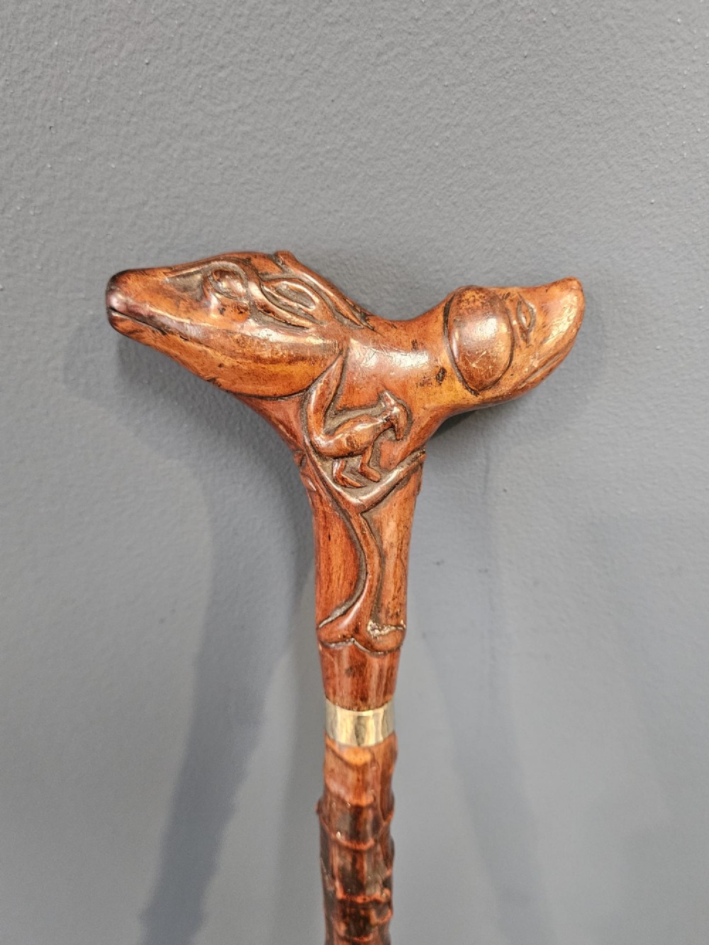 An Edwardian walking stick with a hand-carved wooden dog head handle on a knobbly blackthorn shaft with a silver-coloured collar. View II