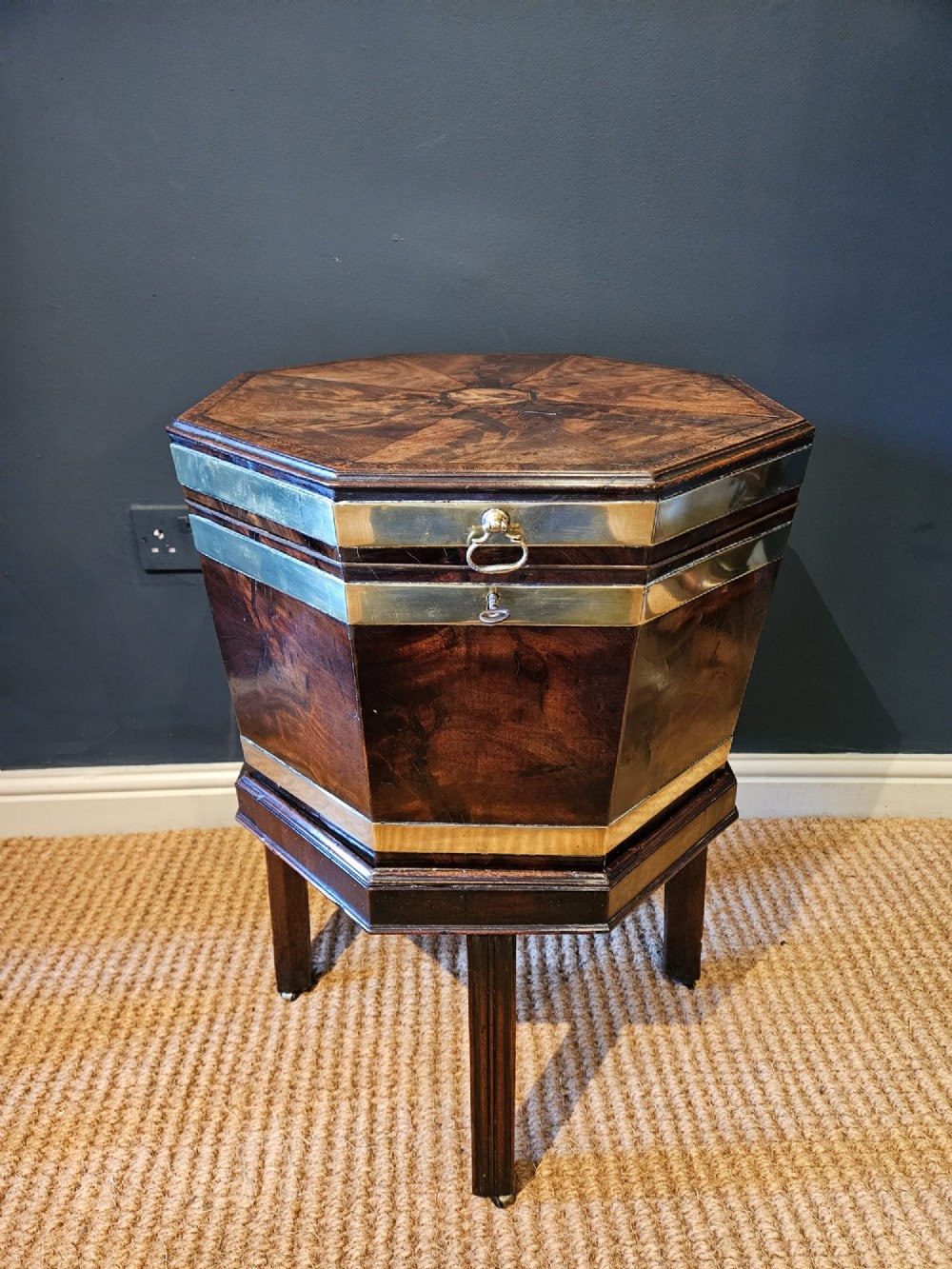 An octagonal George III mahogany wine cooler featuring brass binding bands, a hinged lid with starburst marquetry, and four square tapered legs.