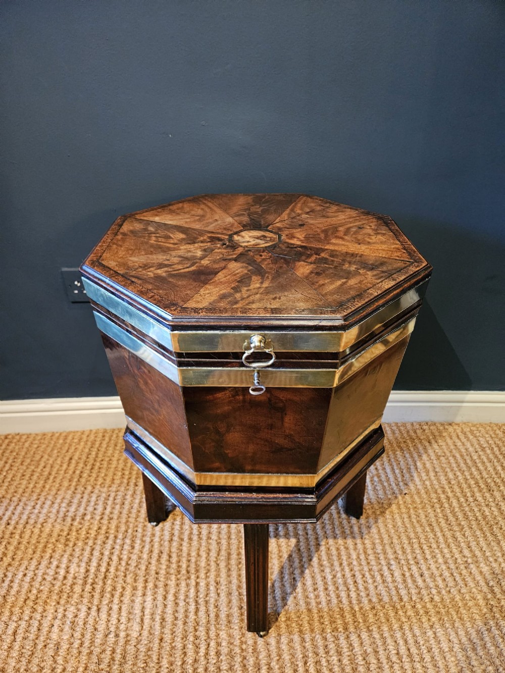 An octagonal George III mahogany wine cooler featuring brass binding bands, a hinged lid with starburst marquetry, and four square tapered legs. View IV