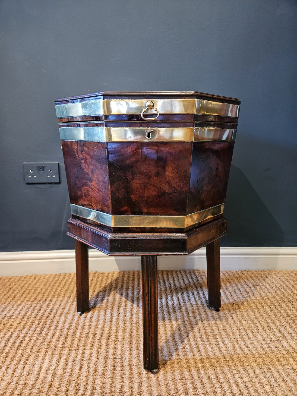 An octagonal George III mahogany wine cooler featuring brass binding bands, a hinged lid with starburst marquetry, and four square tapered legs. View V