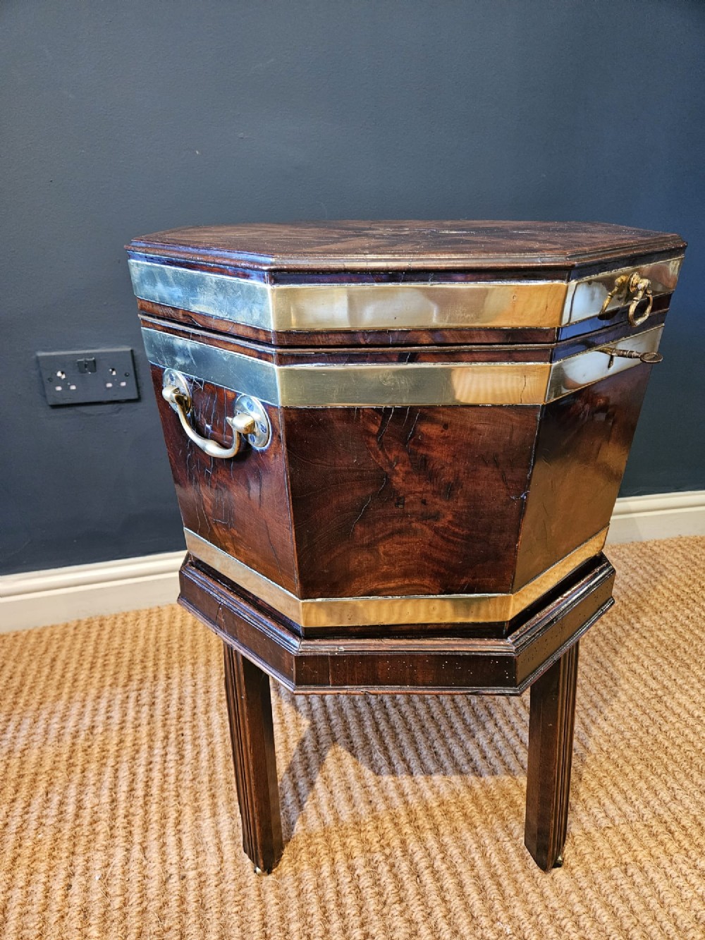 An octagonal George III mahogany wine cooler featuring brass binding bands, a hinged lid with starburst marquetry, and four square tapered legs. View VI