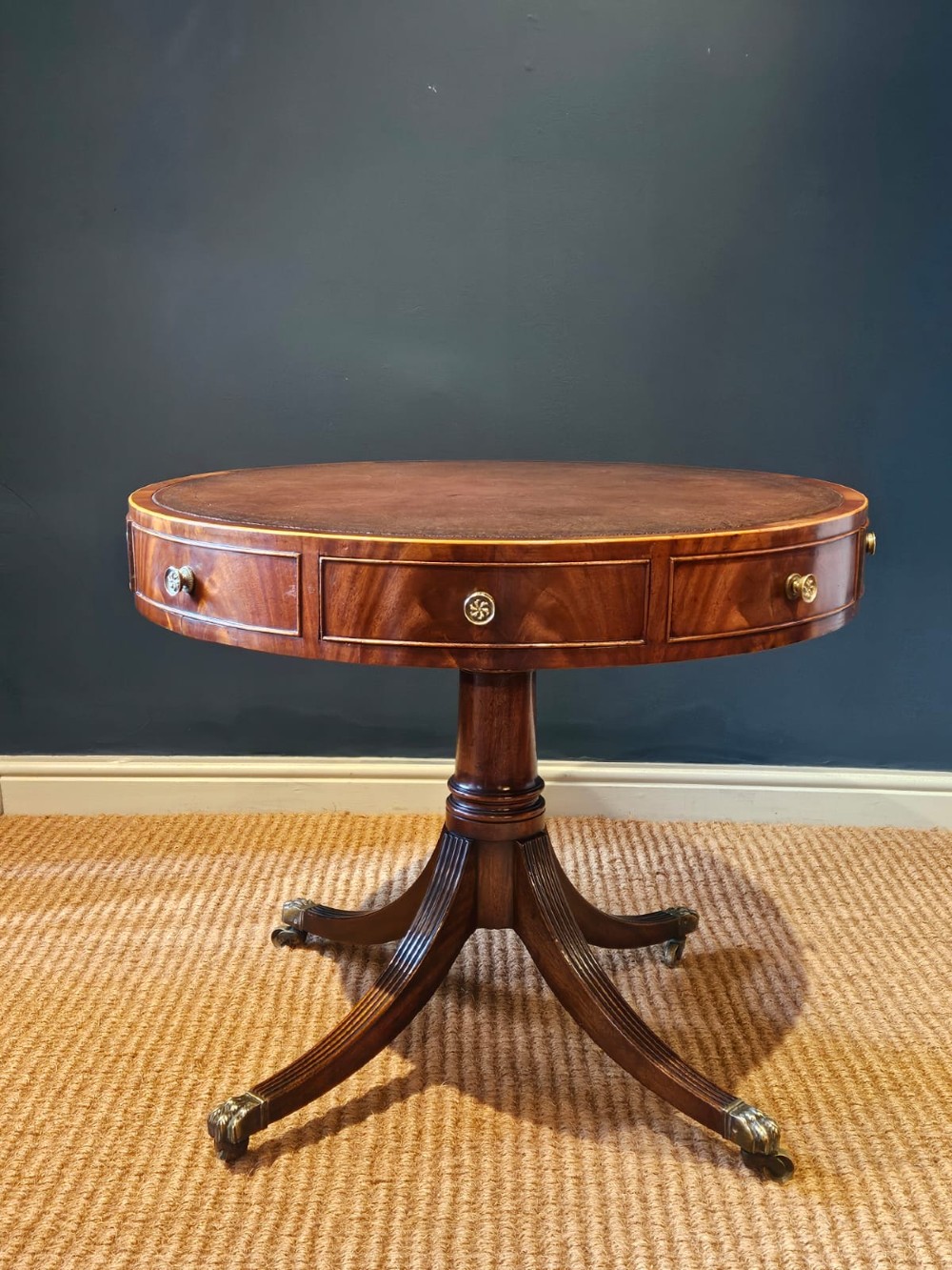 A small circular Regency mahogany drum table with a brown leather inset top, frieze drawers, turned pedestal stem, and reeded splayed legs on brass castors.