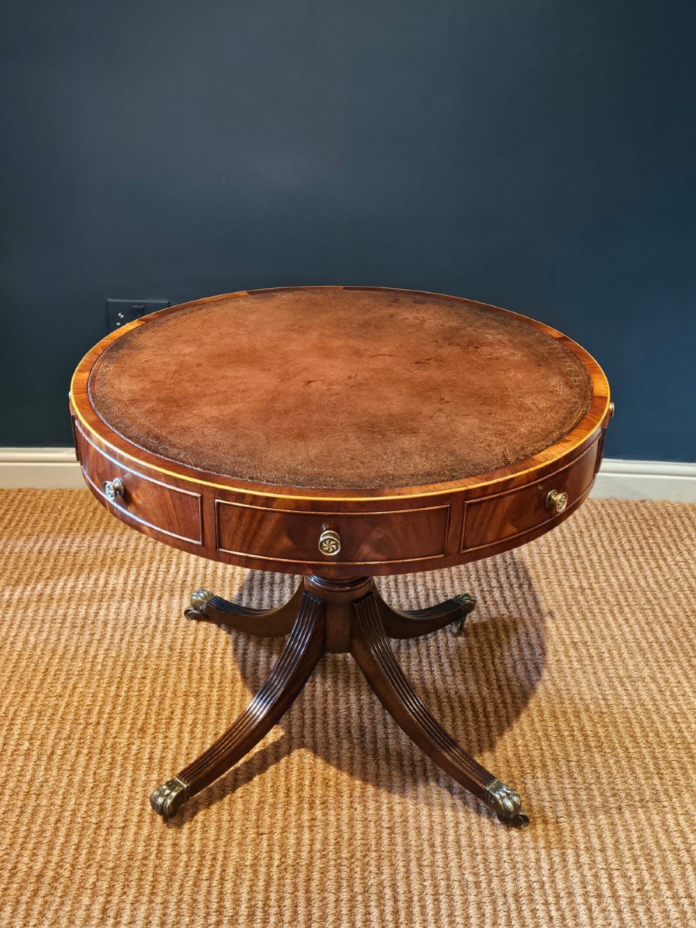 A small circular Regency mahogany drum table with a brown leather inset top, frieze drawers, turned pedestal stem, and reeded splayed legs on brass castors. View VII
