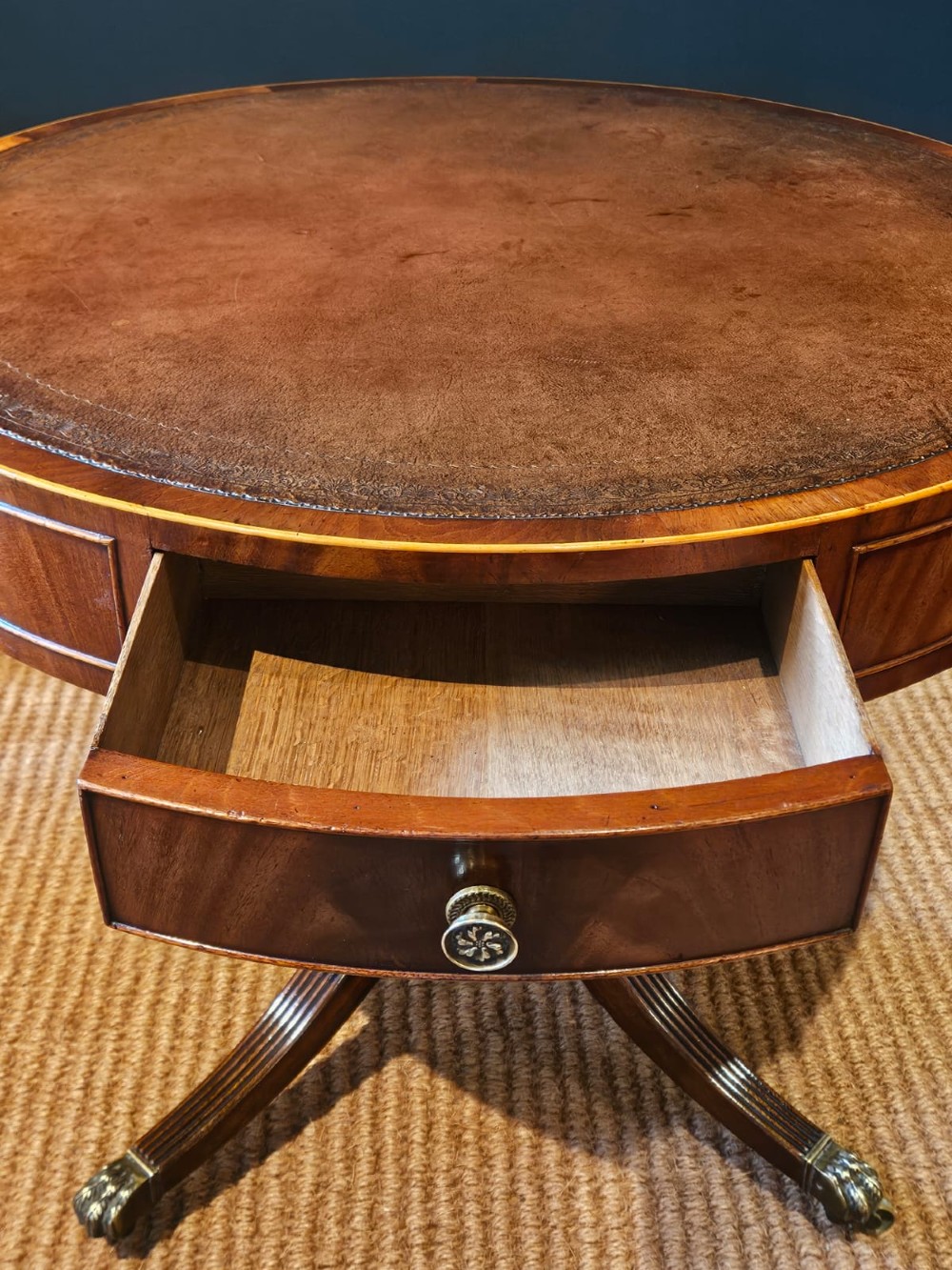 A small circular Regency mahogany drum table with a brown leather inset top, frieze drawers, turned pedestal stem, and reeded splayed legs on brass castors. View VIII