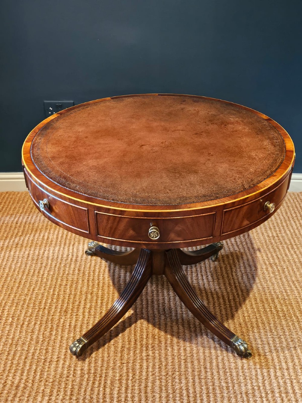 A small circular Regency mahogany drum table with a brown leather inset top, frieze drawers, turned pedestal stem, and reeded splayed legs on brass castors. View IX