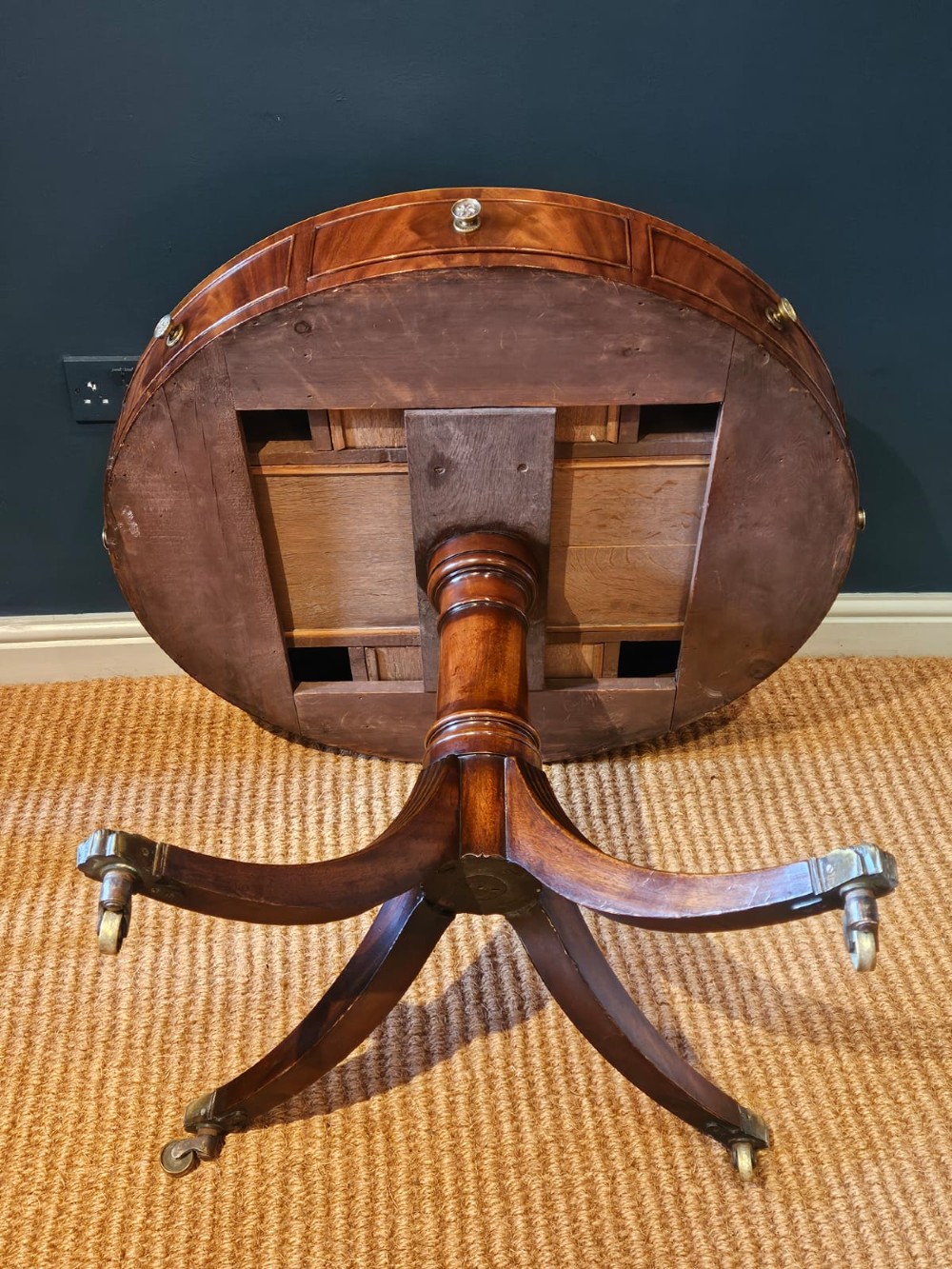 A small circular Regency mahogany drum table with a brown leather inset top, frieze drawers, turned pedestal stem, and reeded splayed legs on brass castors. View X